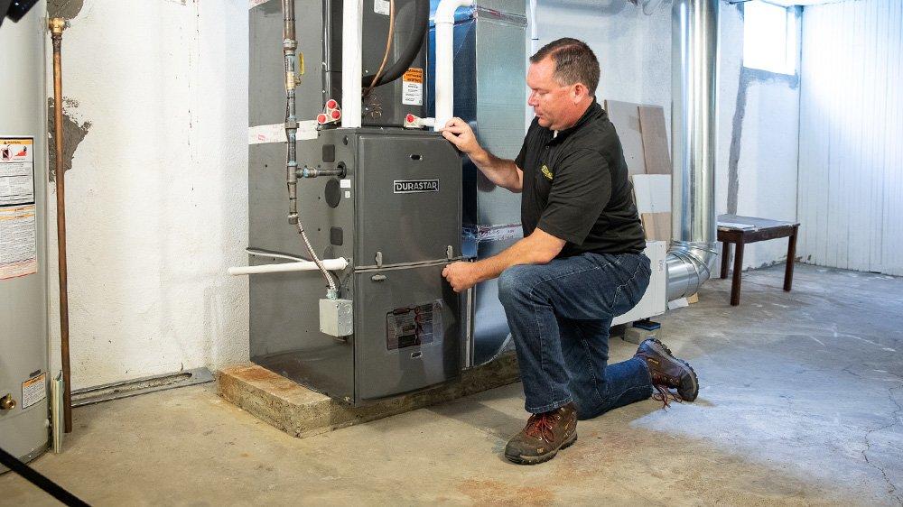 A man kneeling next to an HVAC system in a basement.