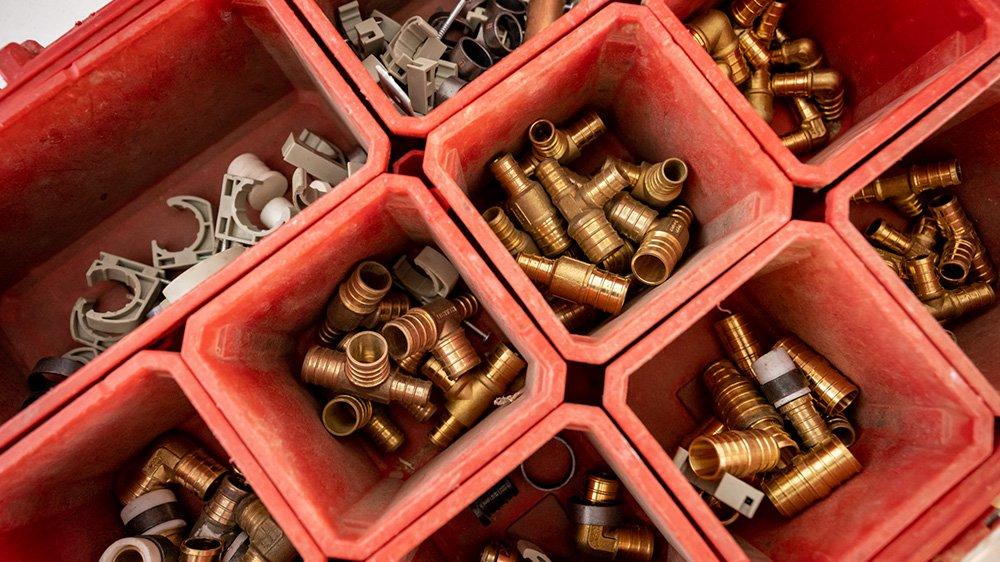 View from above of brass and copper pipe fittings and parts separated into red containers.
