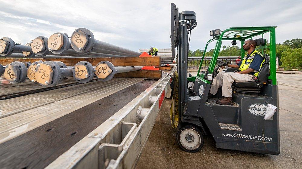 A person in safety gear driving a fork lift with lined pipe